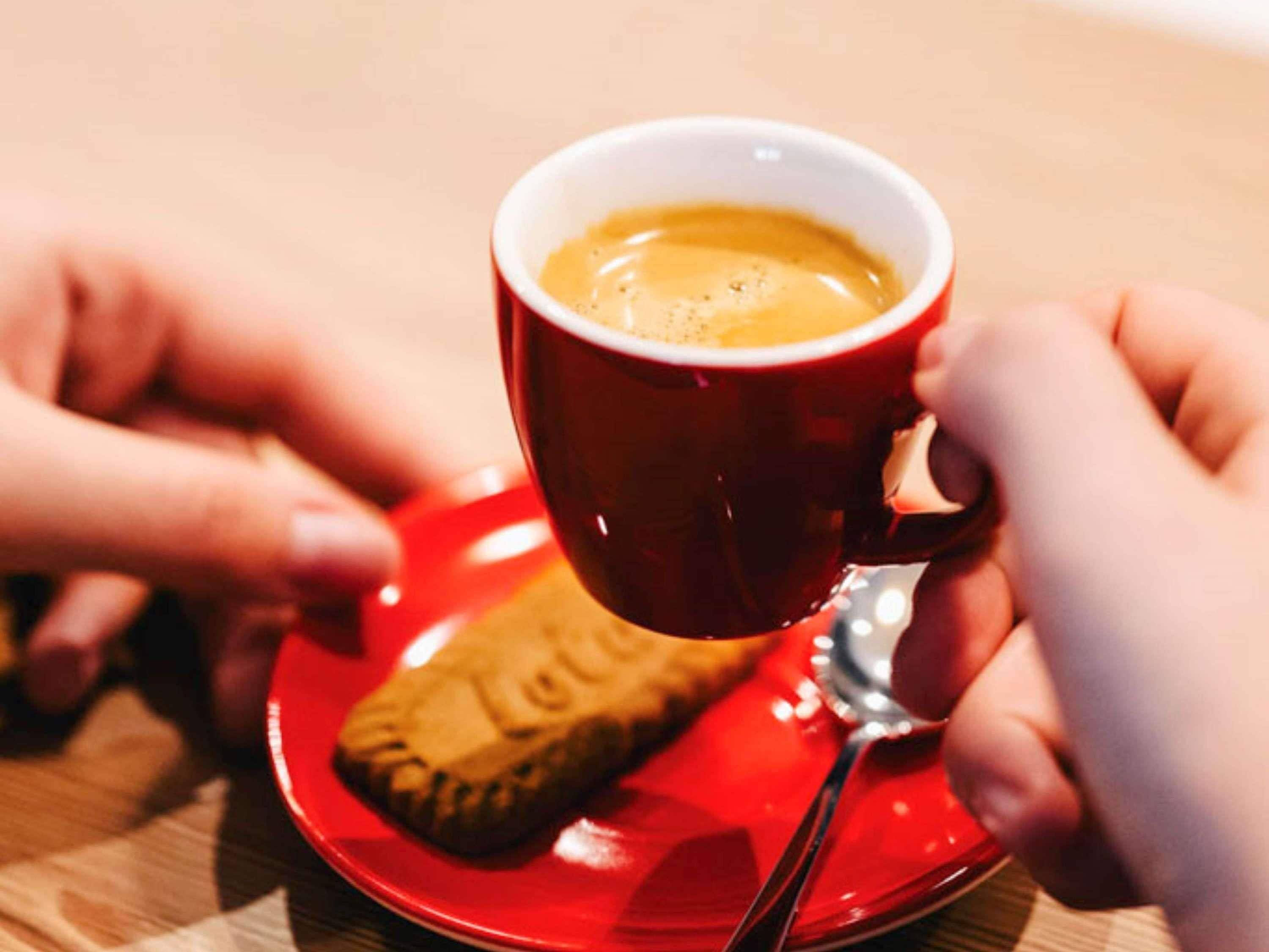 A red cup of coffee with a spoon and a biscuit on a red saucer.
