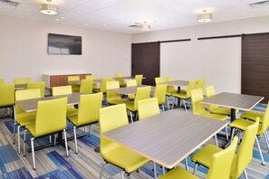 A conference room with multiple tables and chairs, a flat-screen TV mounted on the wall, and a carpeted floor. - Holiday Inn Express & Suites Madison by IHG (Madison)