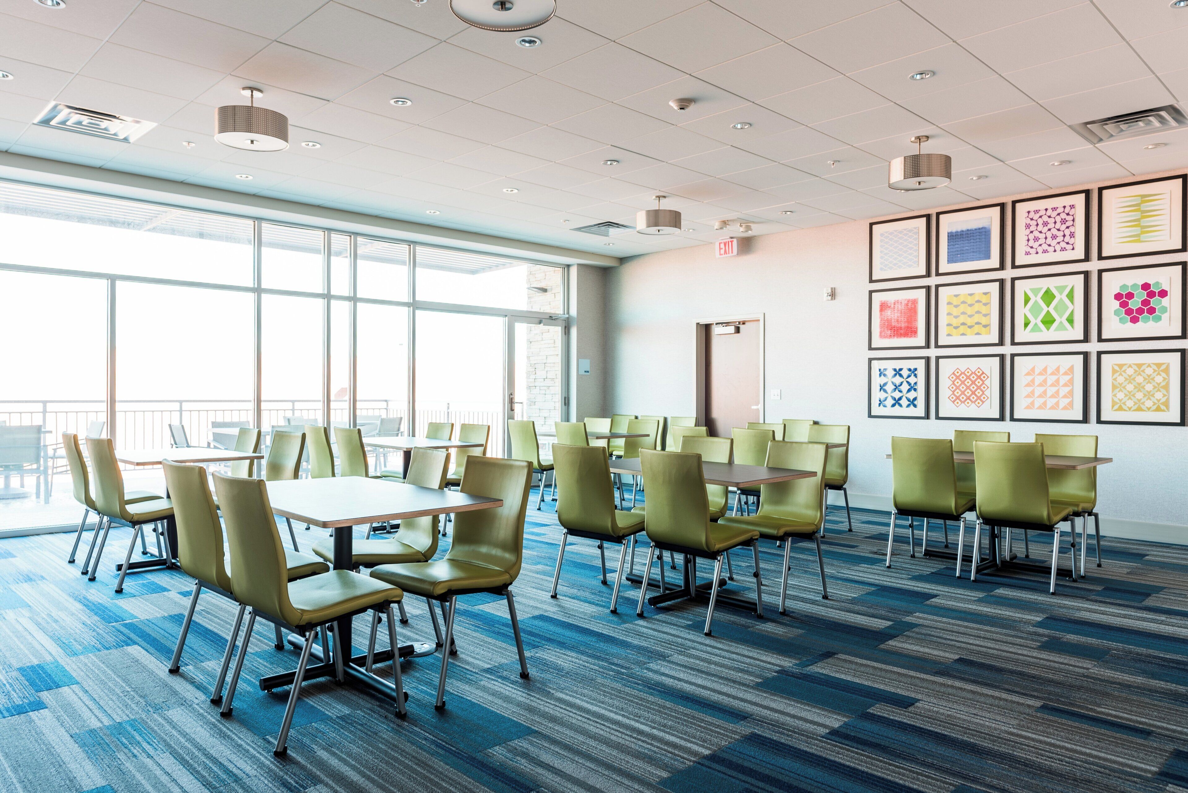 A conference room with tables and chairs, large windows, and a wall with framed artwork.