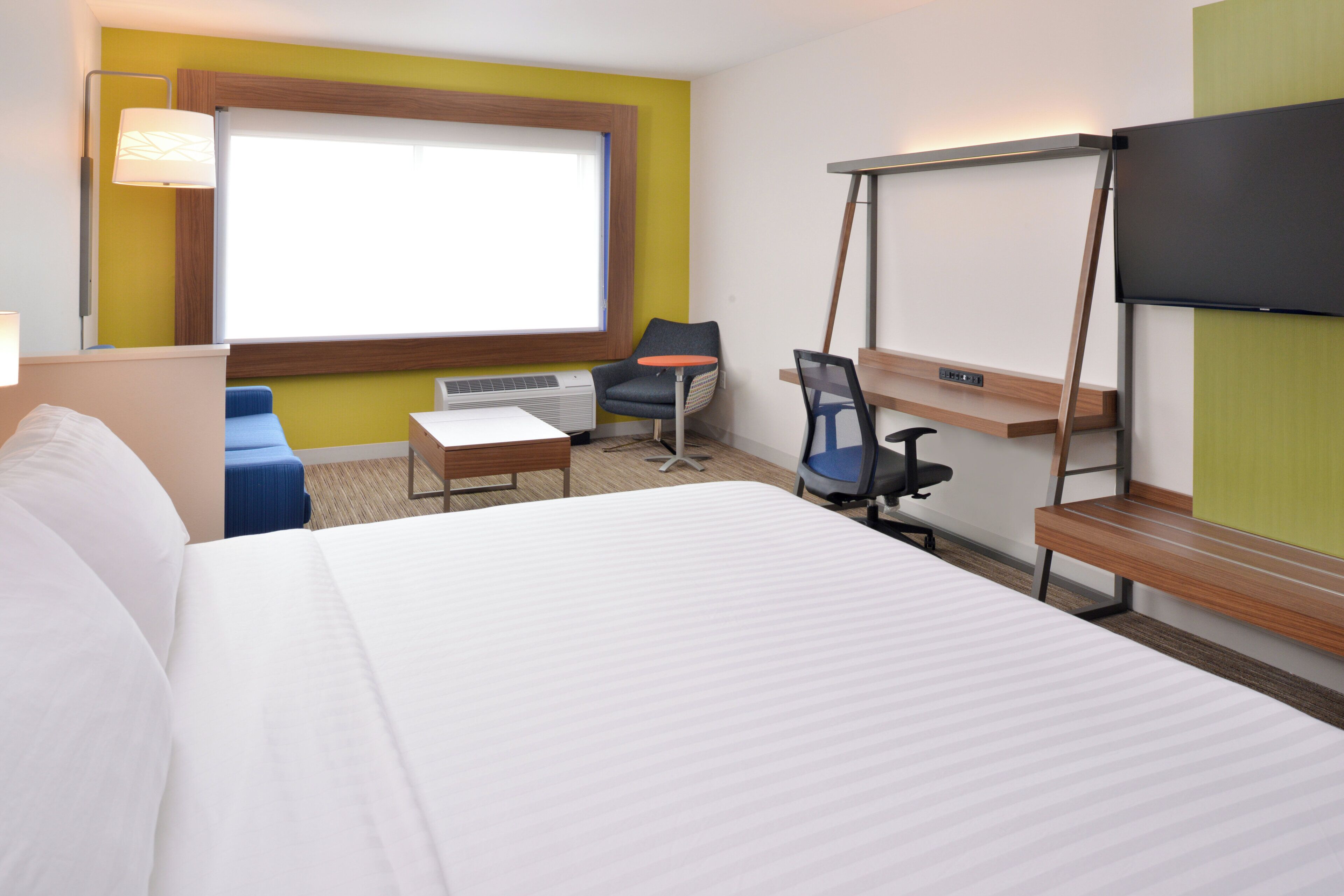 A hotel room with a bed, desk, chair, and a television.