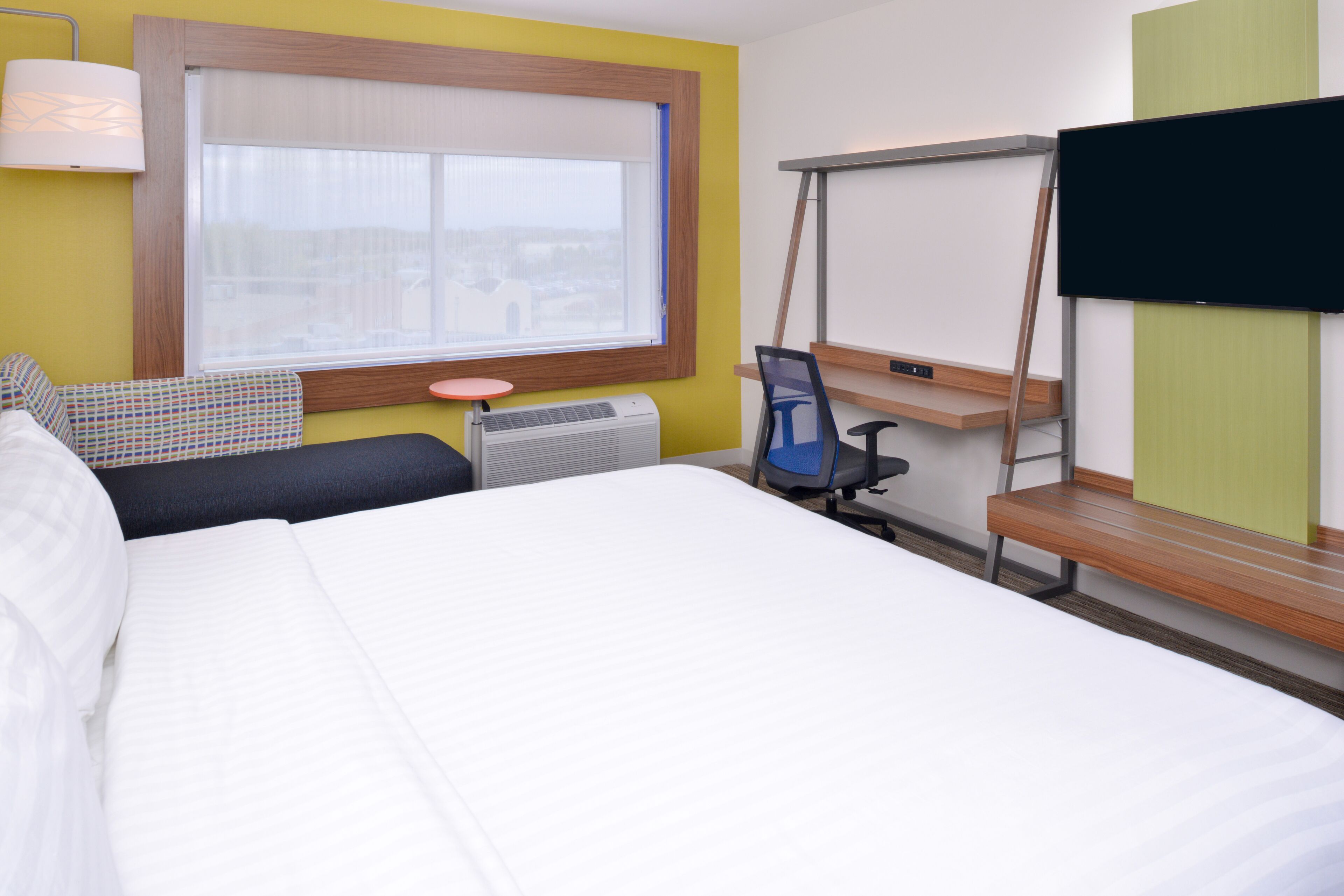 Ein Hotelzimmer mit Bett, Schreibtisch, Stuhl, Fernseher, Fenster und Lampe.