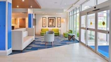 A hotel lobby with a blue and white color scheme, a seating area with a sofa and chairs, and a large window offering a view of the outside.