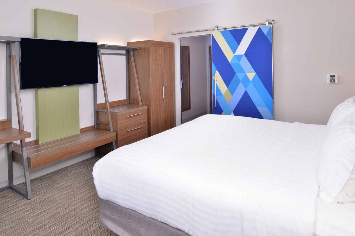 Une chambre d’hôtel avec un lit, un téléviseur fixé sur un meuble, une armoire et une porte de salle de bain.