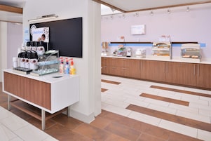 A modern kitchen area with a coffee station, a chalkboard menu, and a buffet counter with food displays.