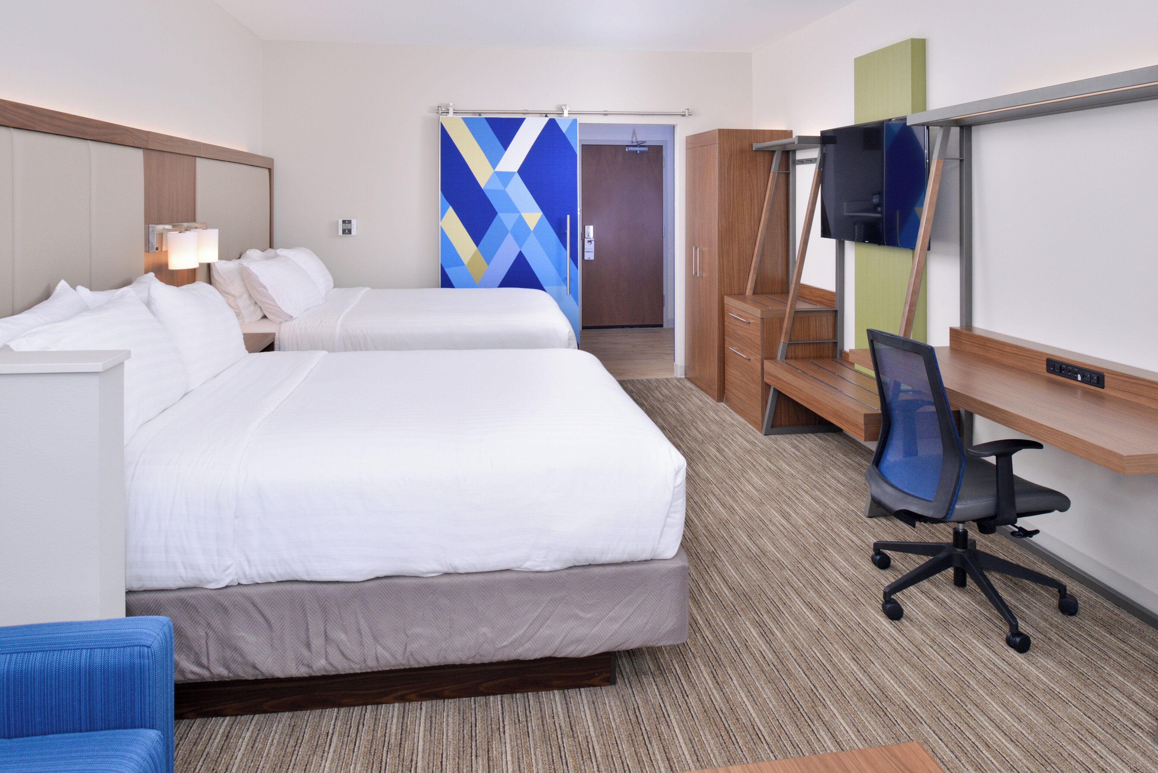 A hotel room with two beds, a desk, a chair, a television, and a wardrobe.