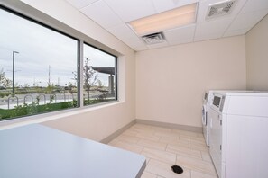 A laundry room with a large window, a washing machine, and a table. - Holiday Inn Express & Suites Madison by IHG (Madison)