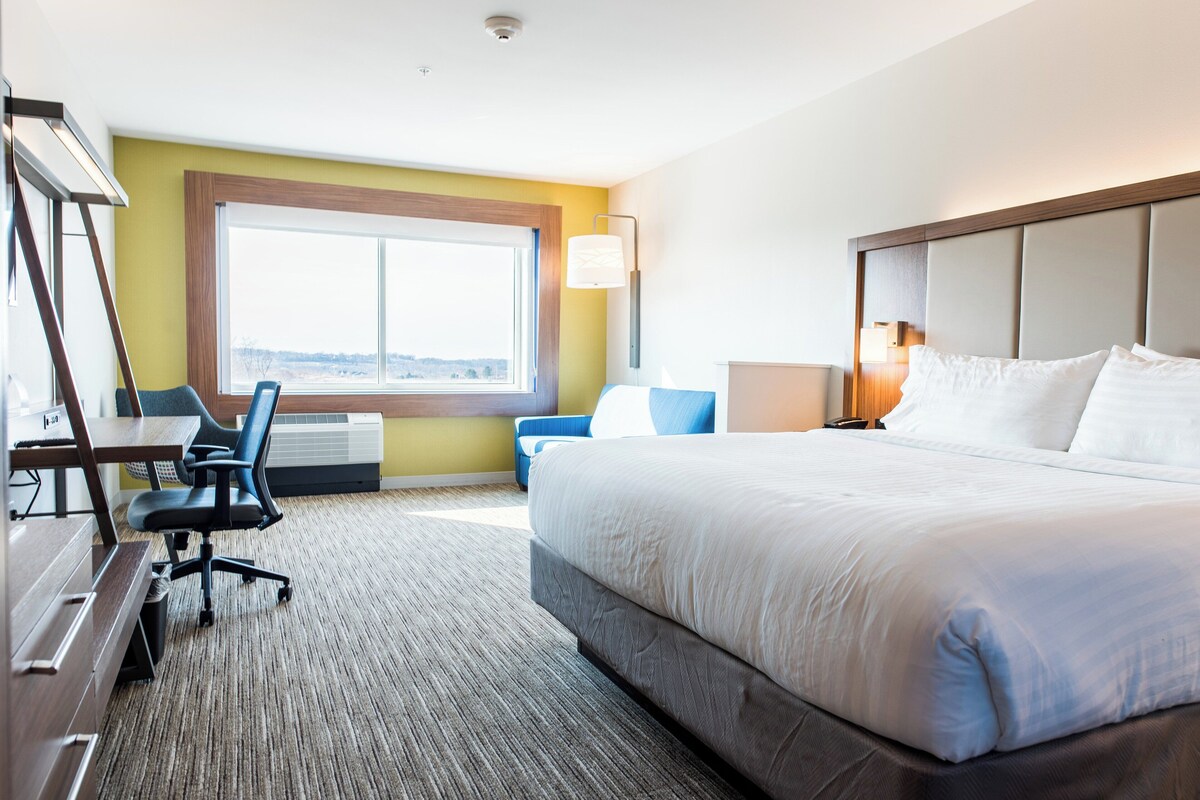 Une chambre d’hôtel avec un grand lit, un bureau avec une chaise, une fenêtre et une lampe.
