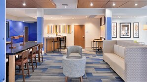 A modern hotel lobby with a dining area, a reception desk, and a seating area with a sofa and armchairs. - Holiday Inn Express & Suites Madison by IHG (Madison)