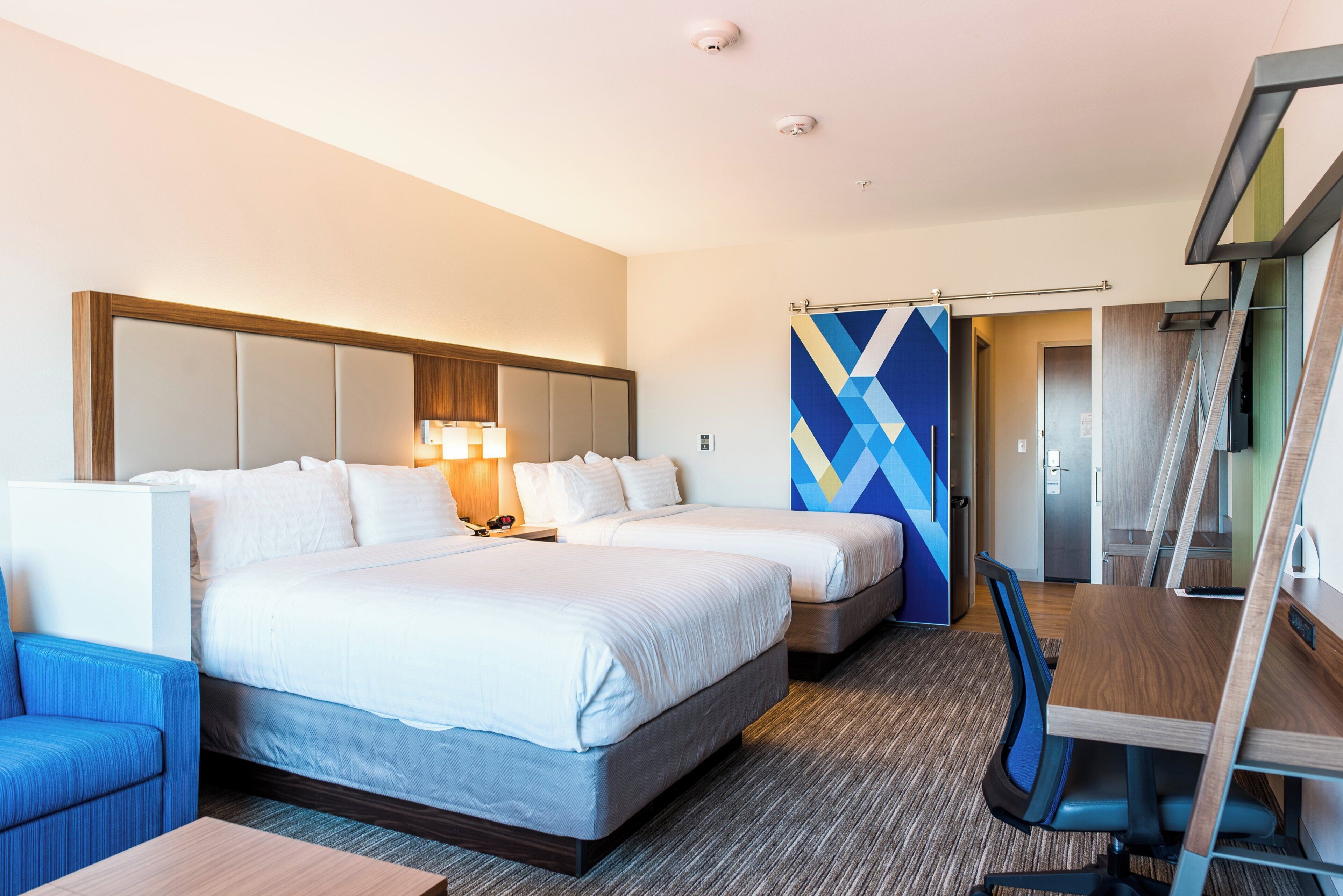 A hotel room with two beds, a desk, a chair, and a bathroom visible through a door.