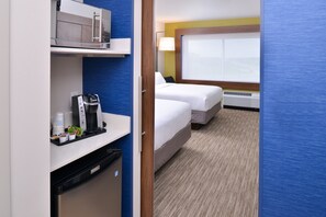 A hotel room with a kitchenette, two beds, a window with a view, and a carpeted floor.