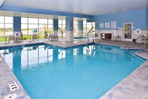 Una piscina interior con agua cristalina, rodeada de sillones de descanso y vistas al exterior.