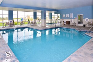 An indoor swimming pool with clear water, surrounded by lounge chairs and a view of the outside.