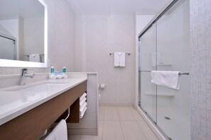 Une salle de bain moderne avec une douche à parois de verre, un lavabo blanc avec un meuble-vasque en bois et un grand miroir.