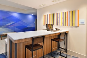 Un mostrador de recepción con una computadora portátil, dos sillas y una pared multicolor a rayas.