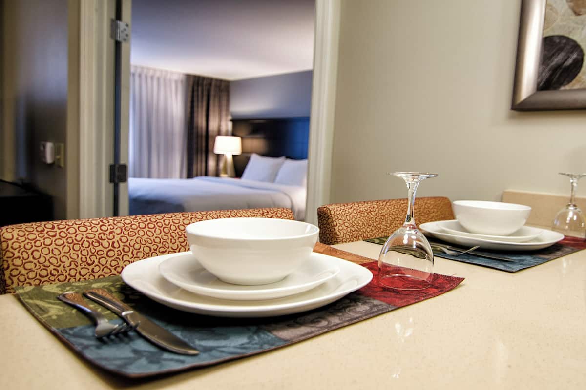 Ein Essbereich in einem Hotelzimmer mit einem Tisch für zwei Personen, gedeckt mit Tellern, Schüsseln, Besteck und einer Weinflasche.