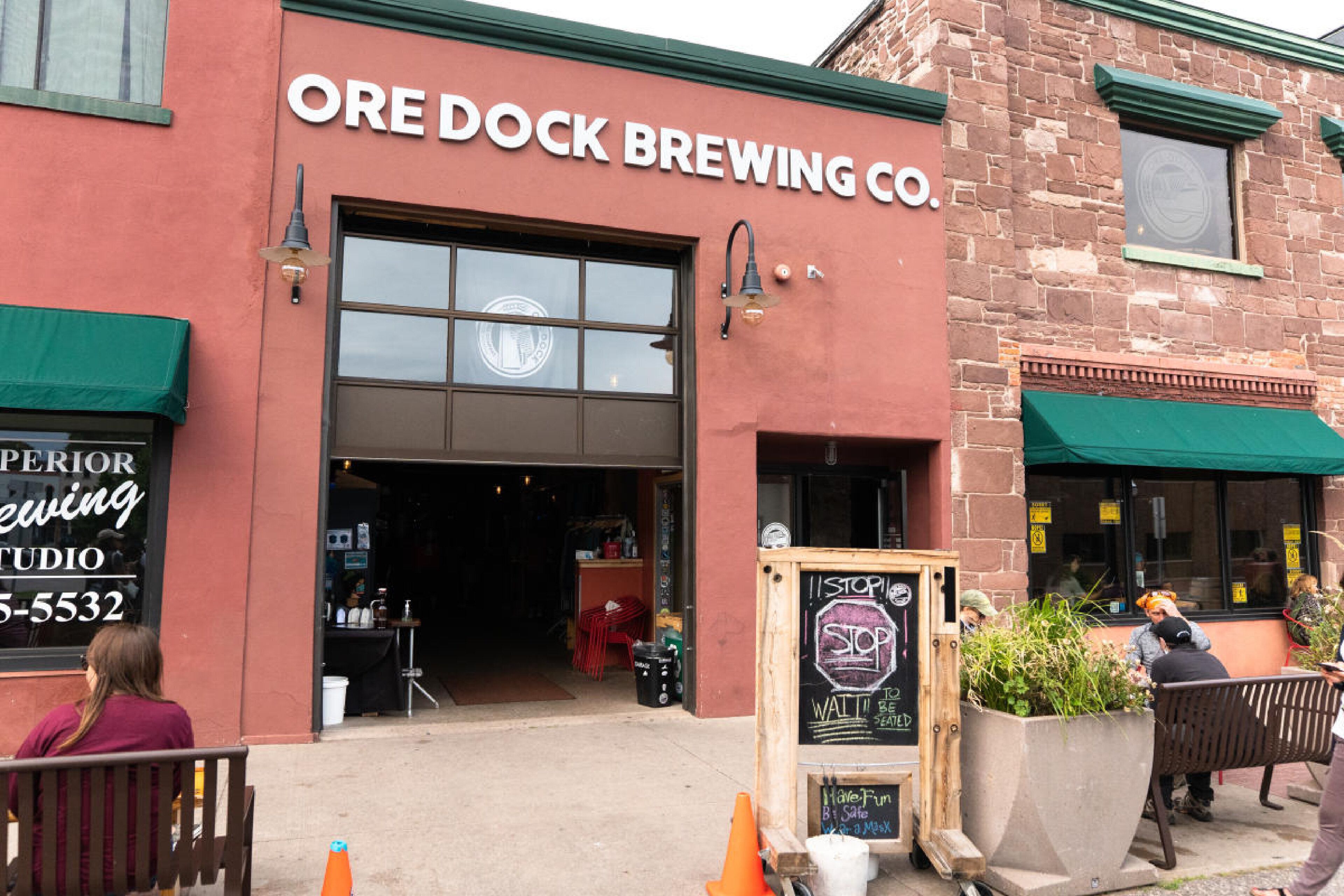 The exterior of Ore Dock Brewing Co. with a large open door, outdoor seating area, and a chalkboard sign.
