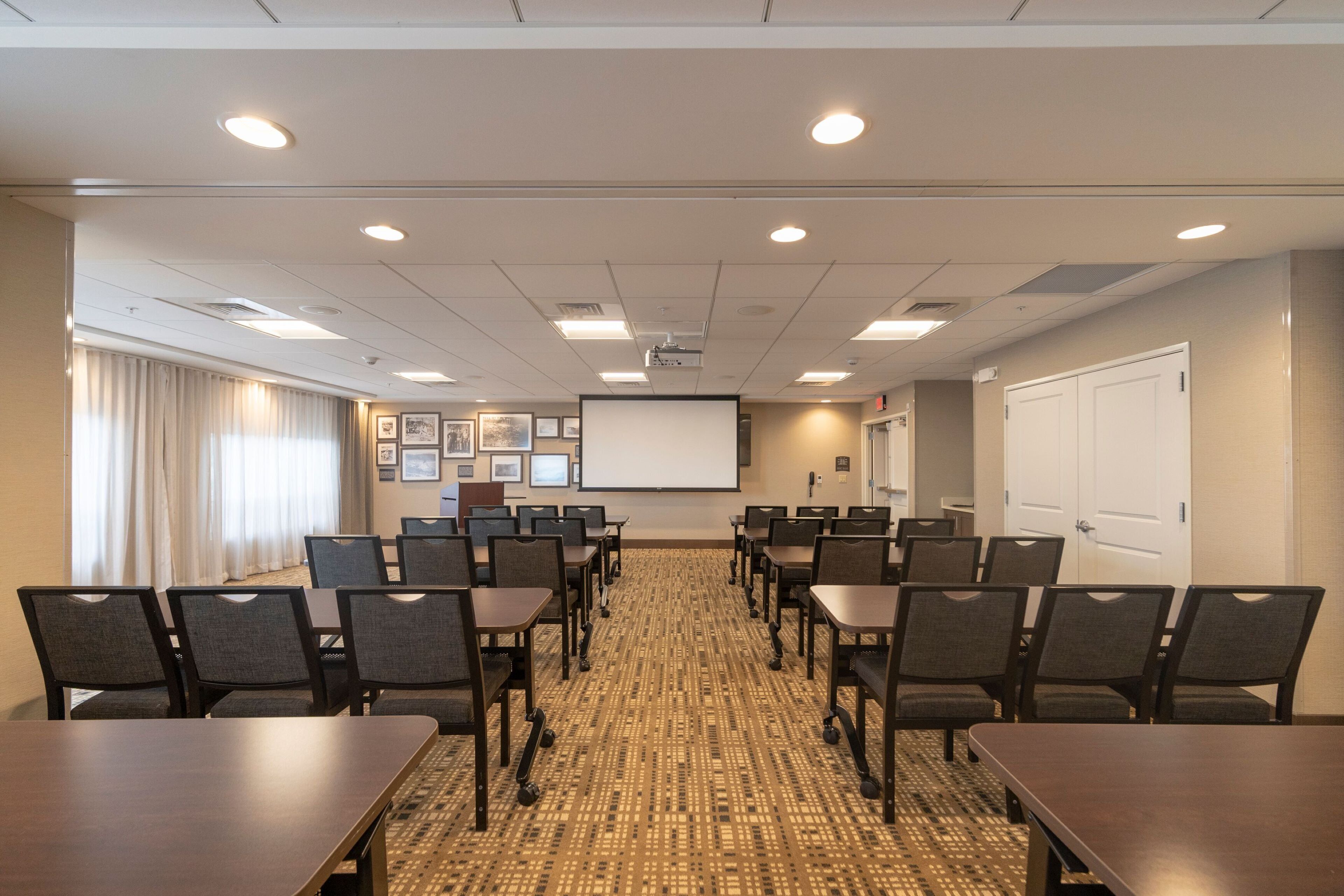 A conference room with a projector screen, multiple tables, and chairs arranged for meetings.