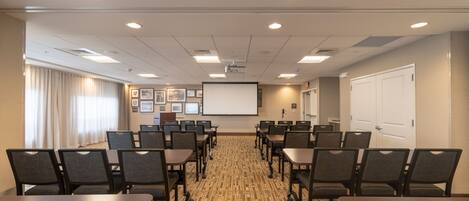 A conference room with a projector screen, multiple tables, and chairs arranged for meetings.