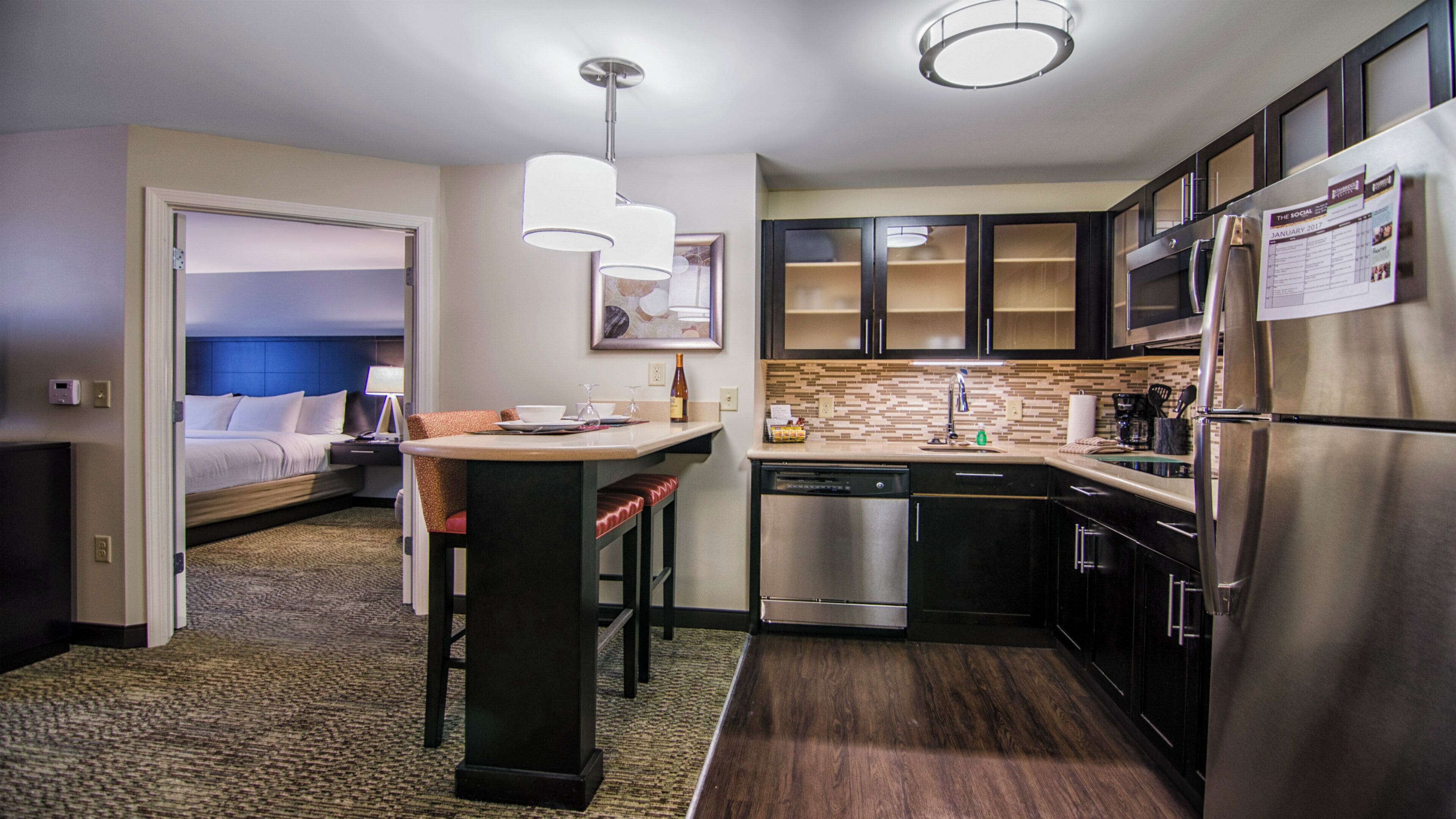 A compact hotel room with a kitchenette, a bed, a sitting area with a table and chairs, and a bathroom.
