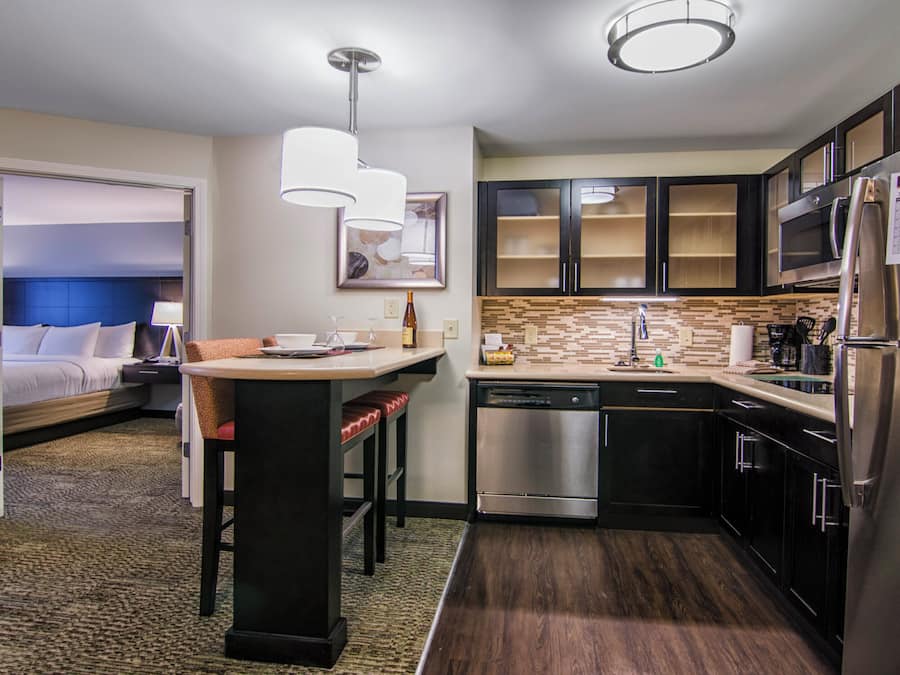 A compact hotel room with a kitchenette, a bed, a sitting area with a table and chairs, and a bathroom.