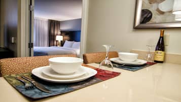 A hotel room dining area with a table set for two, including plates, bowls, cutlery, and a wine bottle.