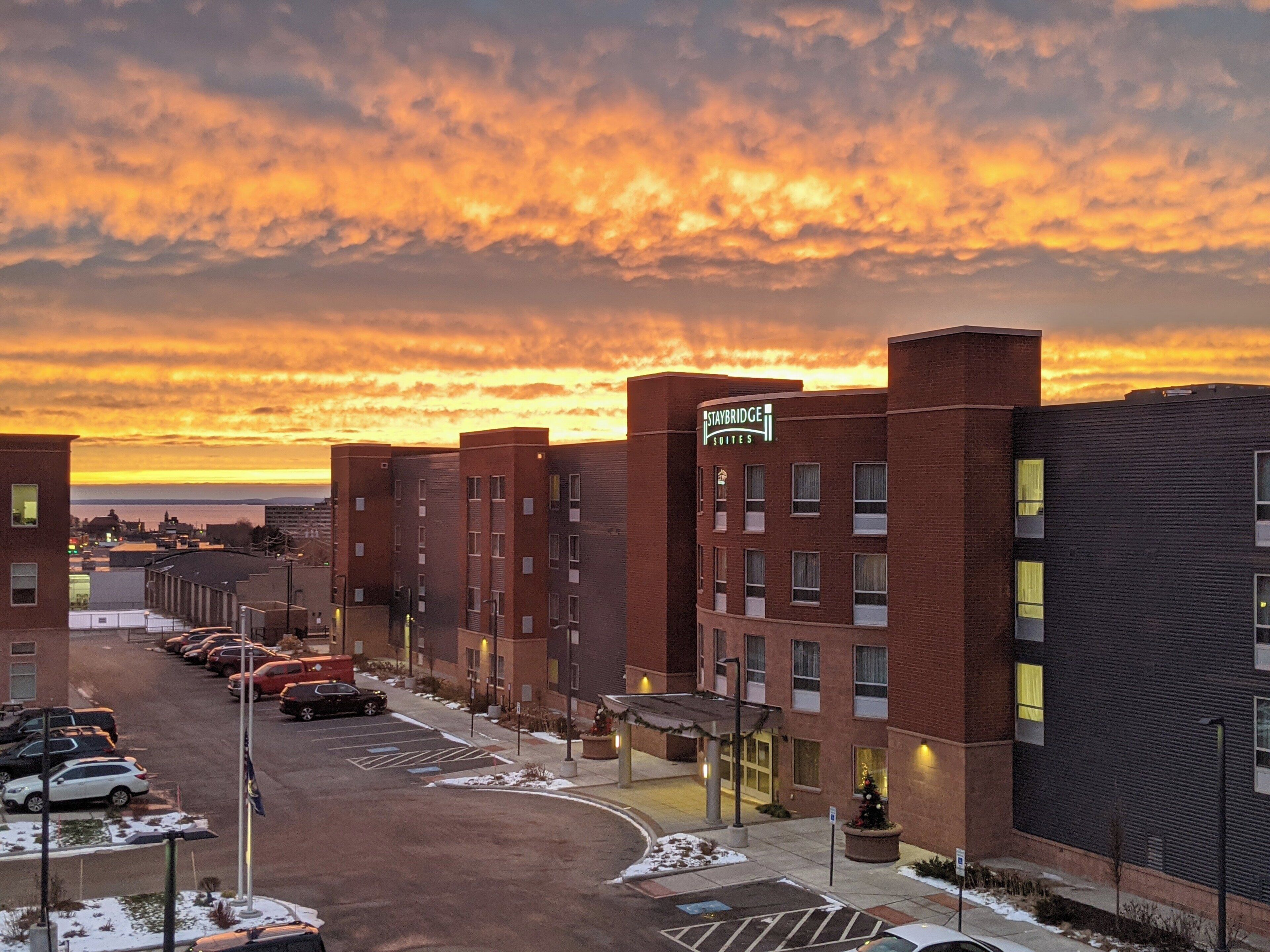 A hotel with a 'Staybridge Suites' sign, a parking lot, and a sunset sky.