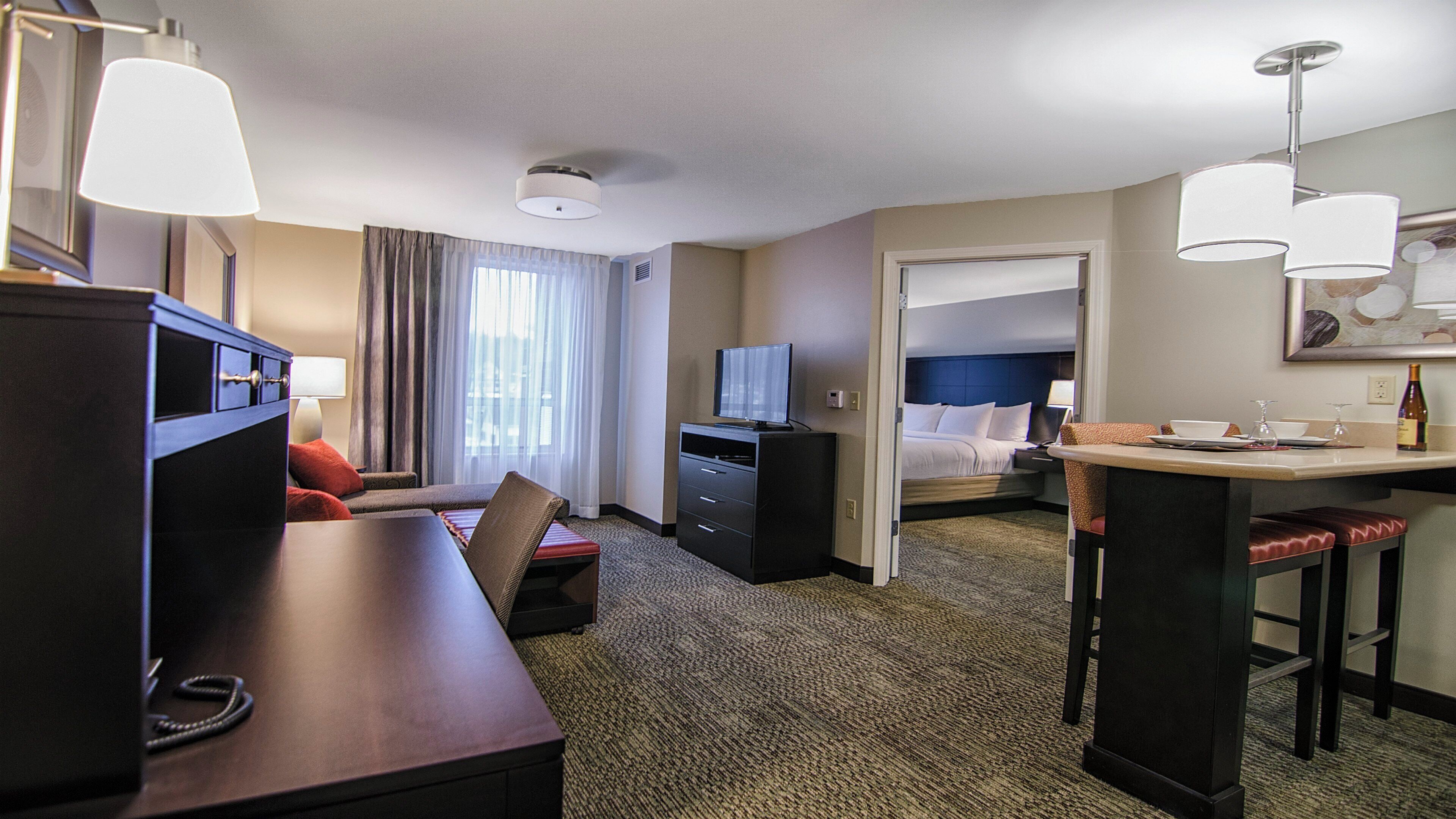 A hotel room with a desk, a bed, a TV, a minibar, and a bathroom visible through an open door.