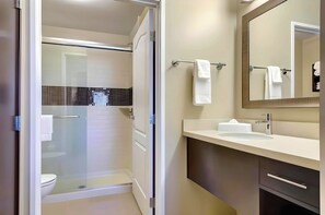 A modern bathroom with a glass-enclosed shower, a white sink, and a mirror with a towel rack.