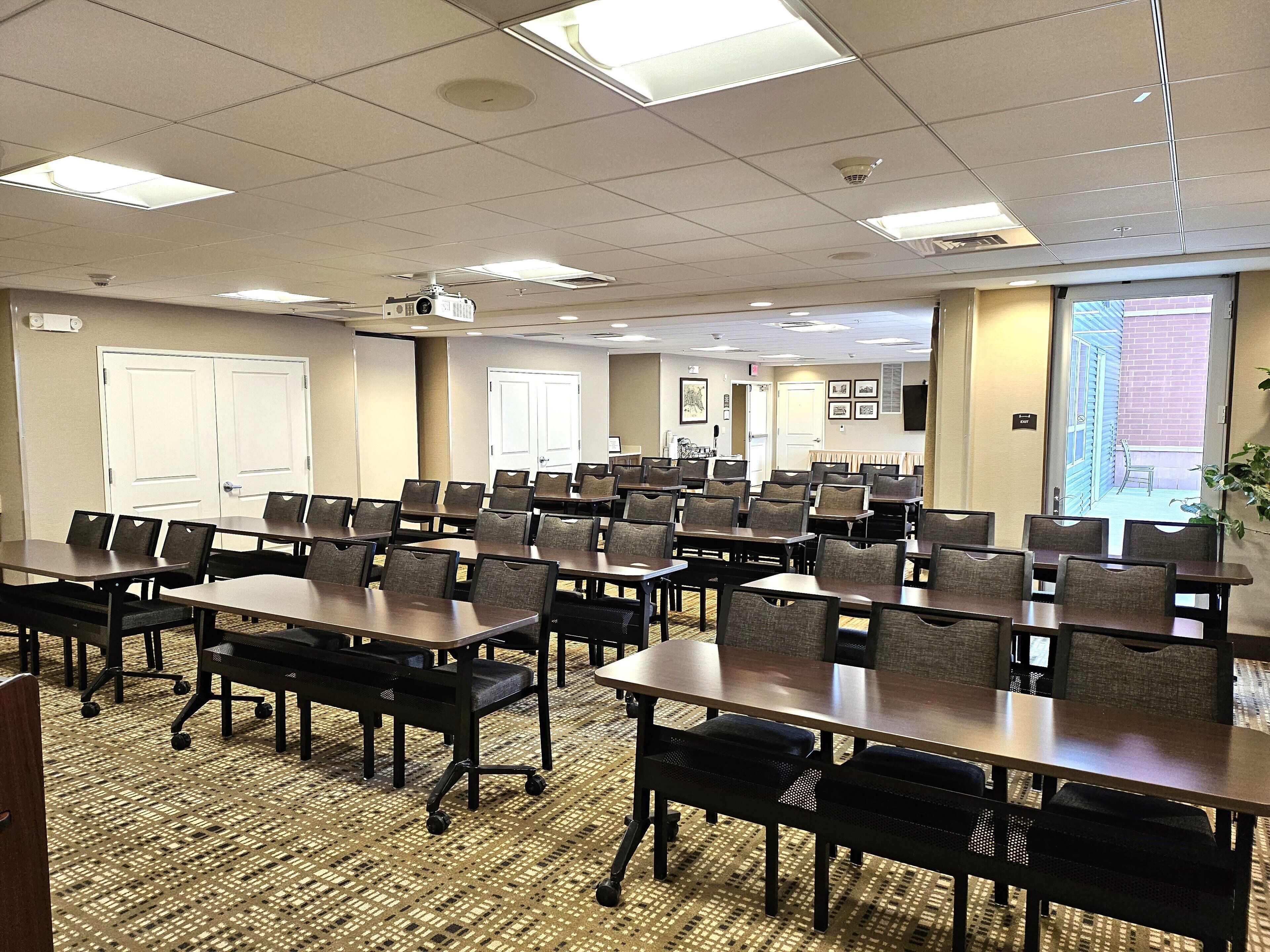 A conference room with multiple tables and chairs, a projector, and a carpeted floor.