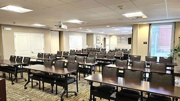 A conference room with multiple tables and chairs, a projector, and a carpeted floor.