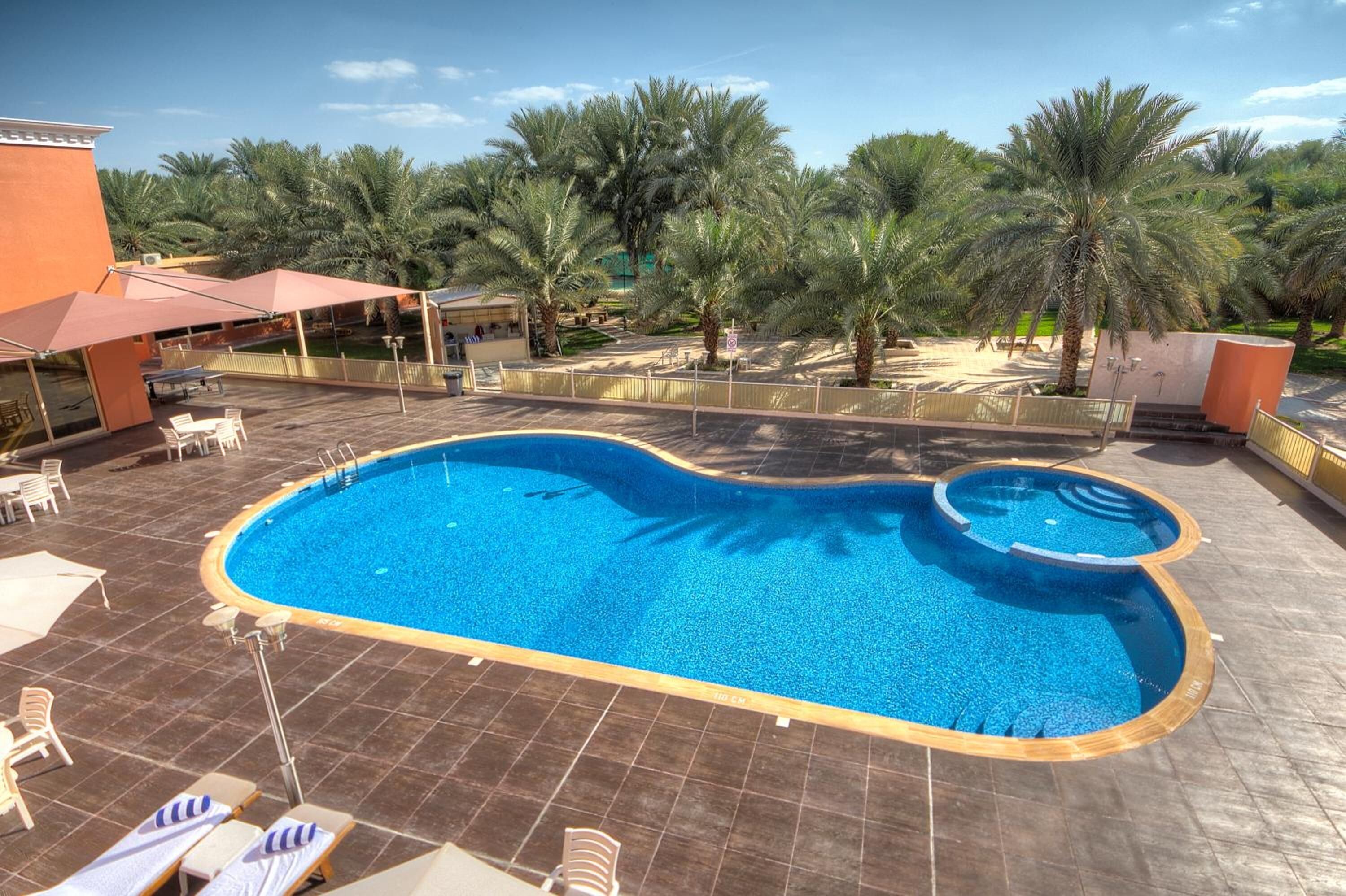 A swimming pool with a unique shape, surrounded by palm trees and outdoor seating.