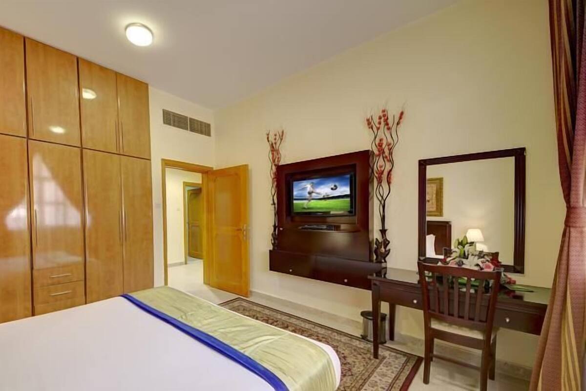 A hotel room with a large bed, wooden wardrobe, flat-screen TV, desk with chair, and a mirror.