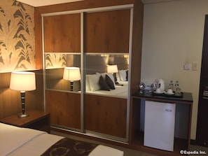 A hotel room with a bed, bedside lamps, a desk with a coffee maker, and a mini-fridge. - GT Hotel Bacolod (Bacolod)