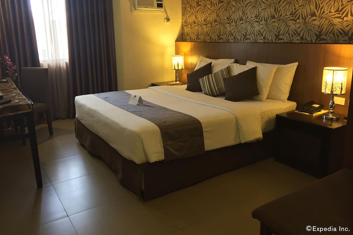 A hotel room with a large bed, two bedside tables with lamps, a desk, and a chair.