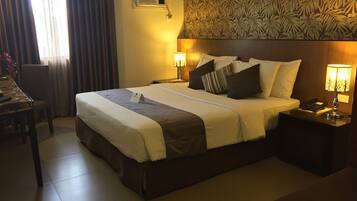 A hotel room with a large bed, two bedside tables with lamps, a desk, and a chair.