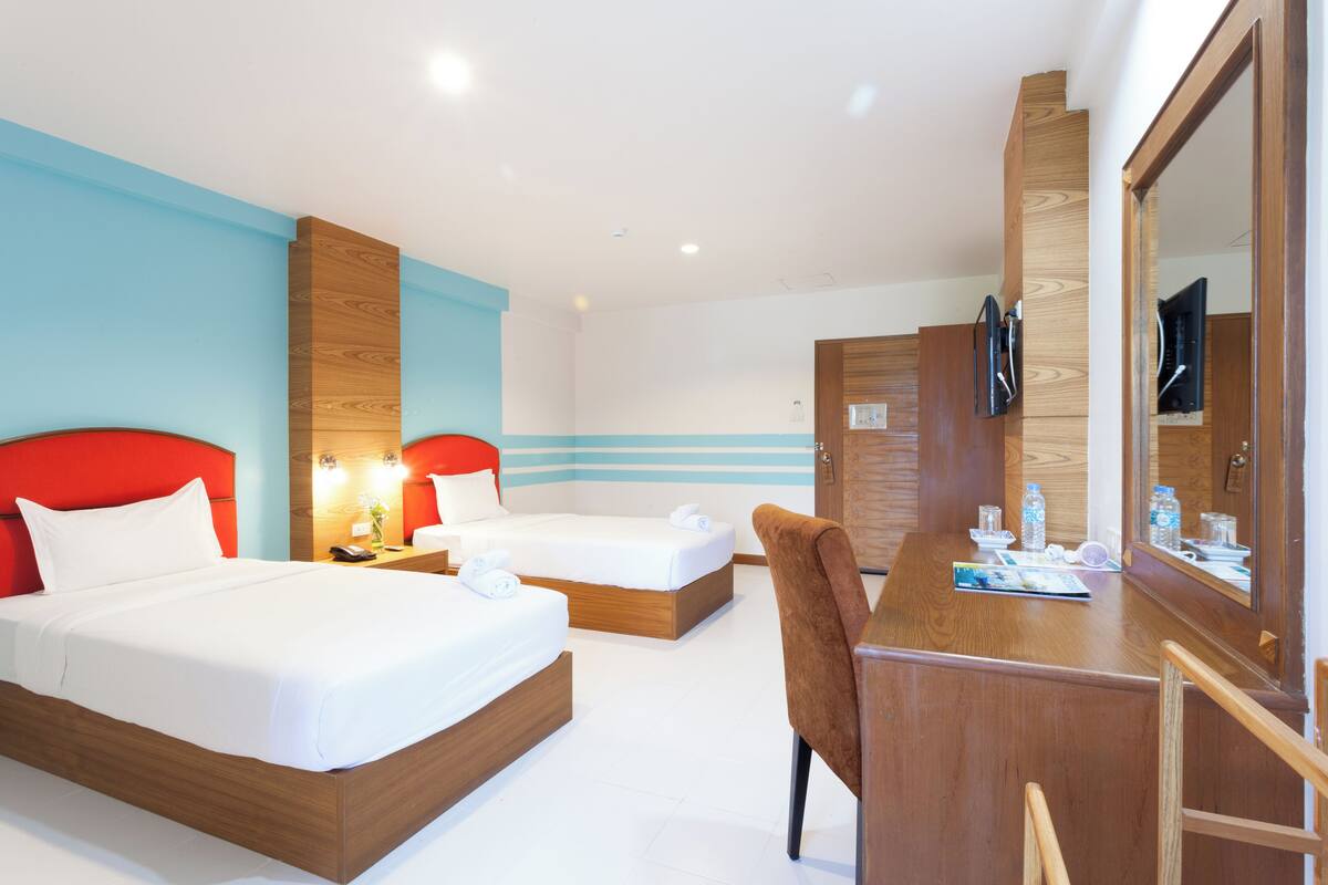 Une chambre d’hôtel avec deux lits, un bureau, une chaise, un miroir et une télévision.