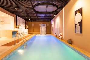 An indoor swimming pool with a modern design, featuring a clear blue water surface, a metal ladder, and a ceiling with a circular skylight. - We Briza Hotel Chiangmai (Chiang Mai)