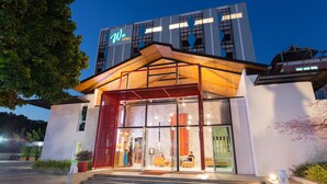Une entrée d’hôtel moderne avec une façade en verre, un auvent rouge et une enseigne sur laquelle on peut lire : « We briza ».