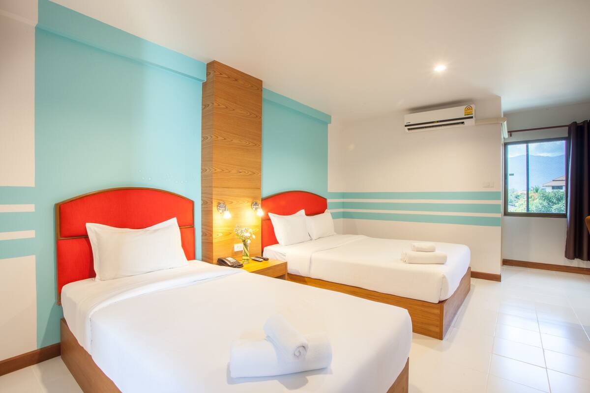 Une chambre d’hôtel avec deux lits, un mur décoratif en bois, une fenêtre avec des rideaux et un appareil de climatisation.