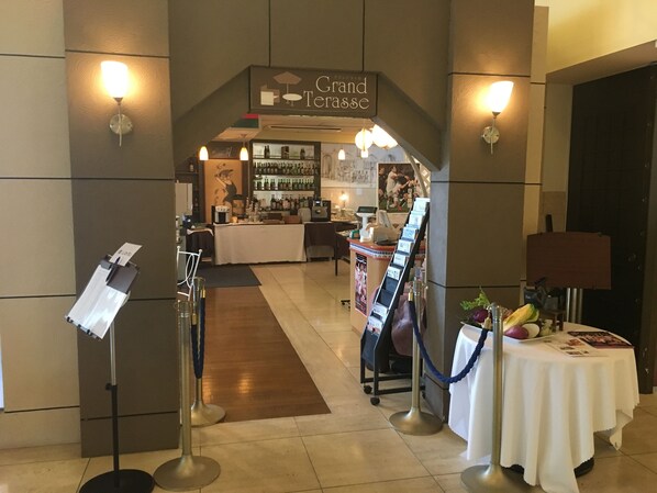 A hotel lobby with a reception desk, a bar area, and a seating area with a table set for a meal.