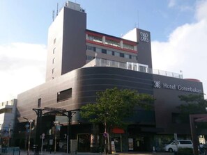 A modern hotel with a prominent 'Hotel Gotenbakan' sign, a large entrance canopy, and a parking area visible in the foreground.