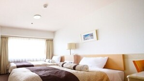 Una habitación de hotel con dos camas, una mesita de noche, una lámpara y un ventanal con cortinas.