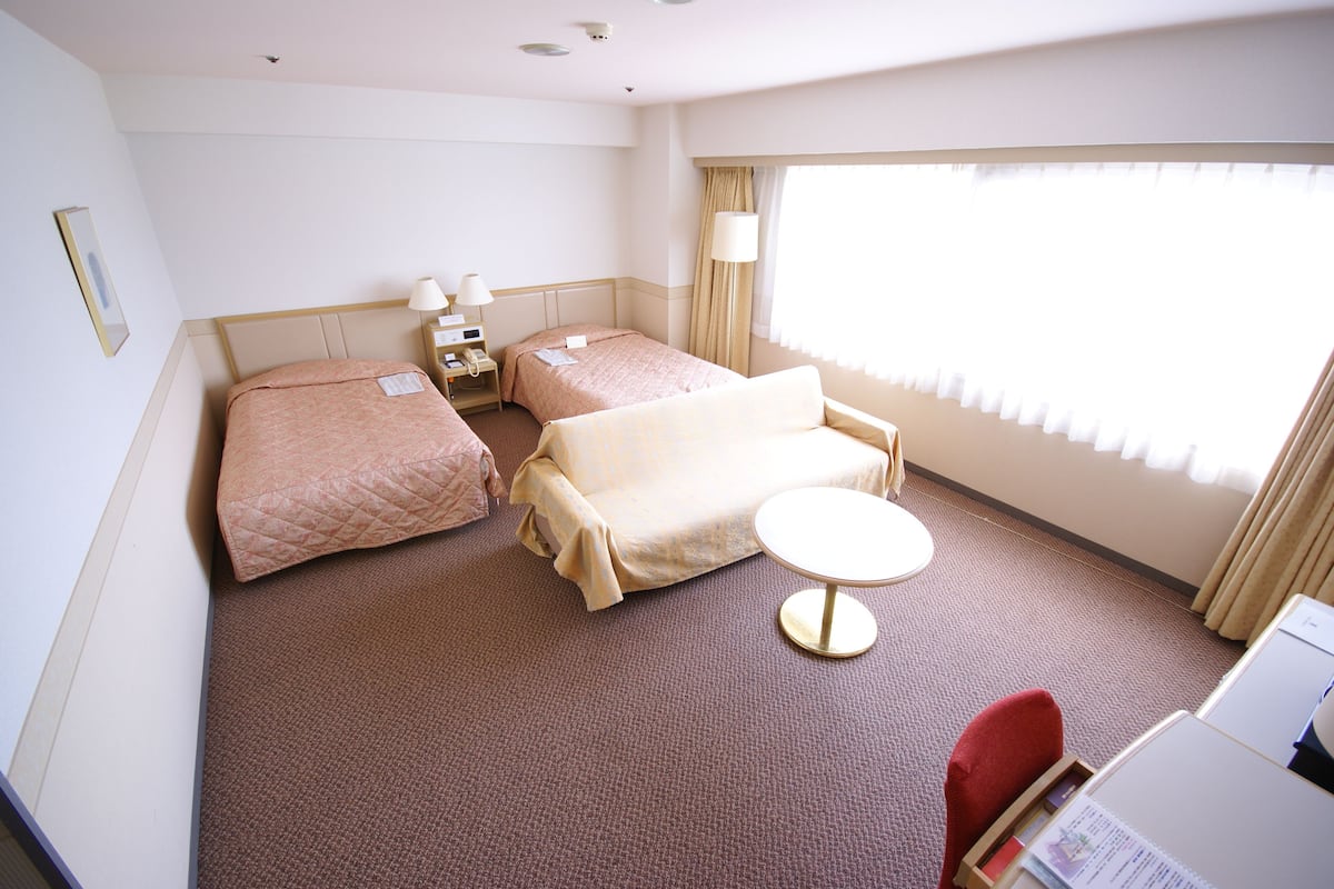 A hotel room with two beds, a sofa, a small table, and a desk with a computer.