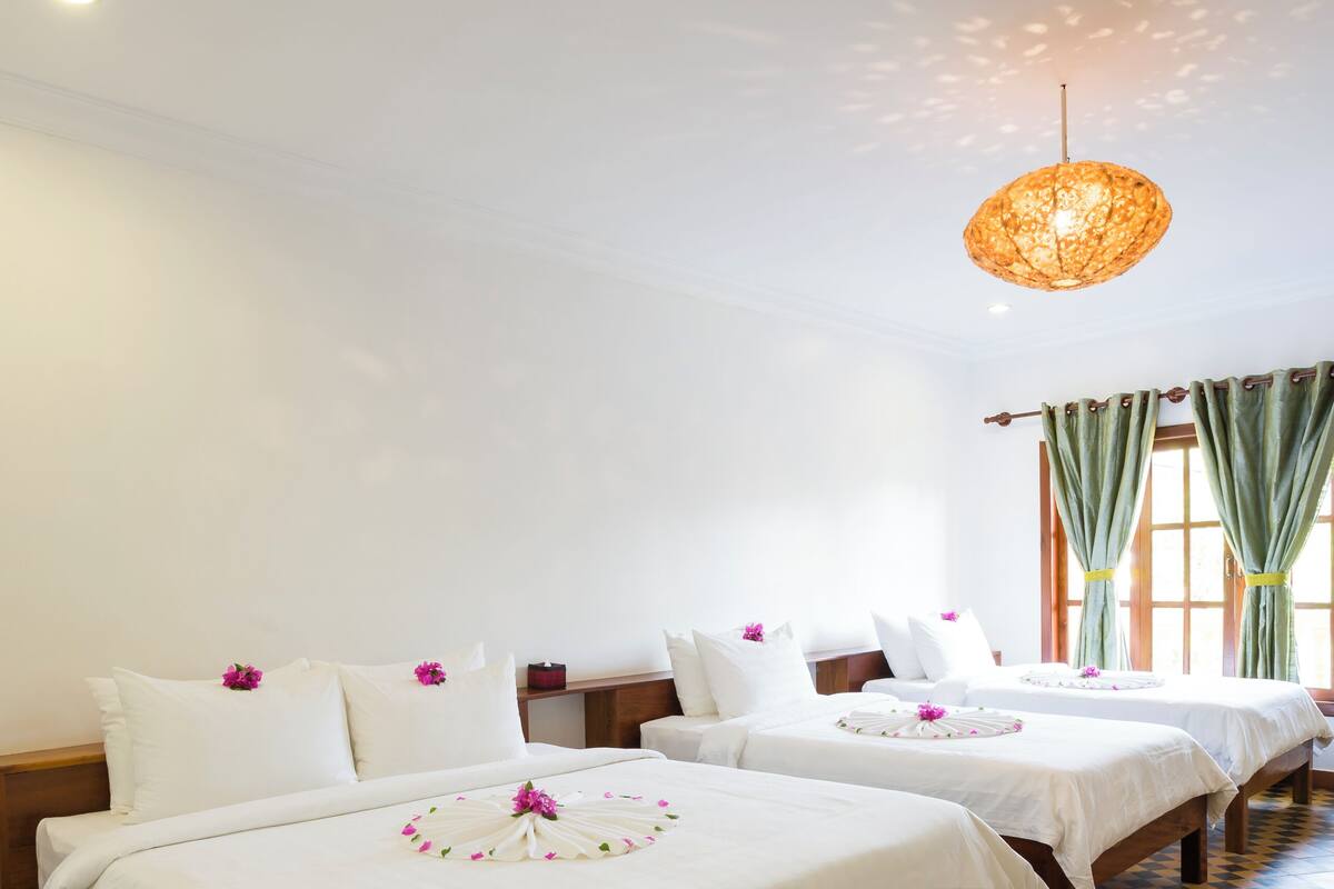 Une chambre d’hôtel avec deux lits, un sol à carreaux, un luminaire suspendu et une fenêtre avec des rideaux.