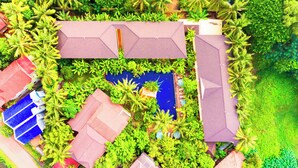 Vue aérienne d’un complexe hôtelier comprenant plusieurs bâtiments, une piscine et une végétation luxuriante.