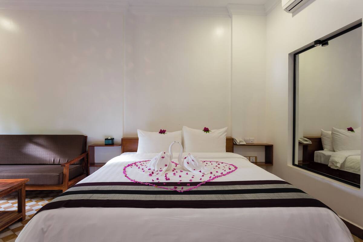 Une chambre d’hôtel avec un grand lit, une chaise en bois, une table de chevet et un miroir au mur.