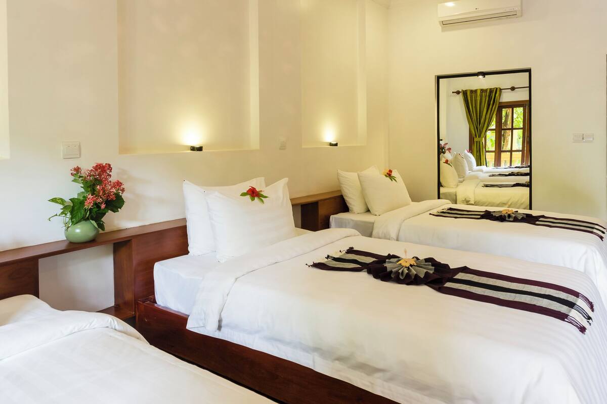 Une chambre d’hôtel avec deux lits, un grand miroir, un luminaire suspendu et un vase avec des fleurs.
