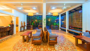 Un hall d’entrée spacieux, doté d’un tapis à motifs, de meubles en bois et offrant une vue sur un jardin tropical grâce à de grandes fenêtres.