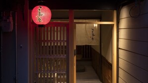En traditionell japansk entré med en träport, en röd lykta och en gång av plattor som leder inåt.