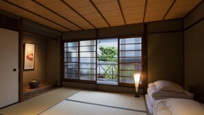 Ett traditionellt japanskt rum med tatamimattor på golvet, en futonmadrass, skjutbara shojidörrar och utsikt över grönskan utanför.